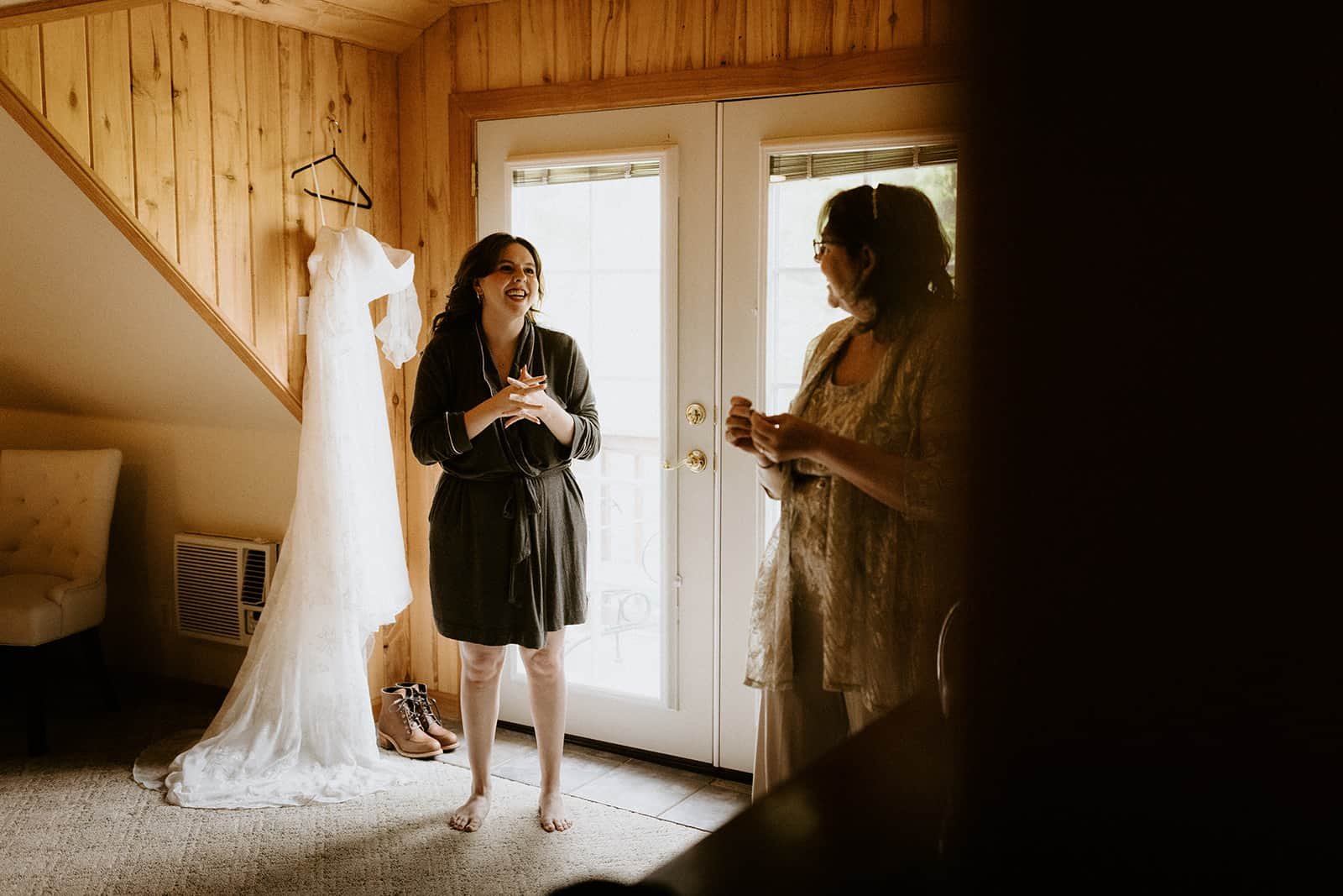 a woman and her mom stand smiling in front of her wedding dress