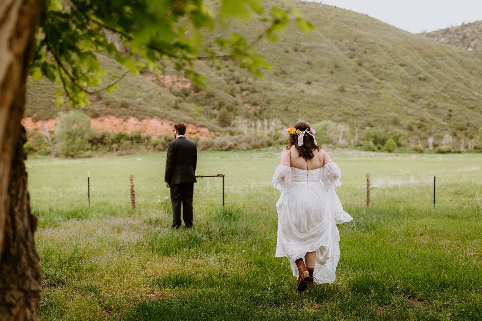 A woman in a wedding dress walks toward a man whose back is toward her