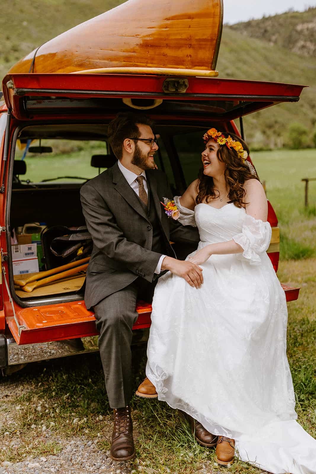 A man and woman sit on the tailgate in their wedding clothes in a red Toyota Land Cruiser