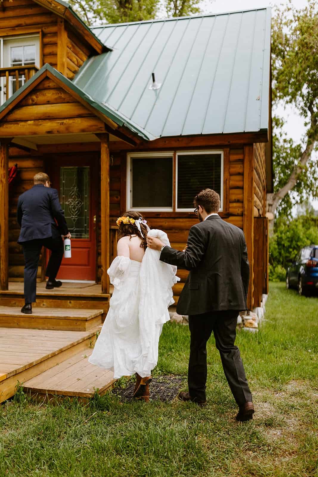 A man helps carry the bottom of a wedding dress into a cabin
