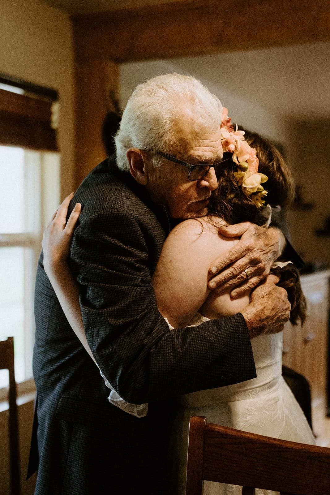 An elderly man embraces a woman in a wedding dress and flower crown