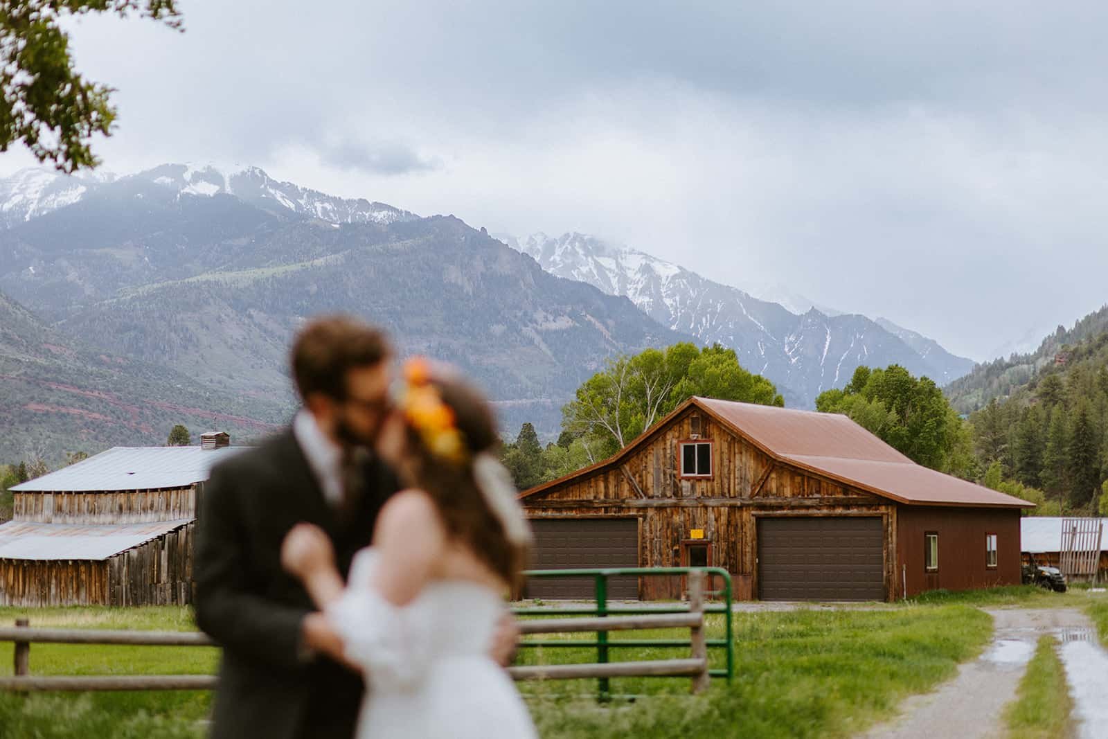 A man and woman kiss in front of a barn and the Sneffles range in Colorado