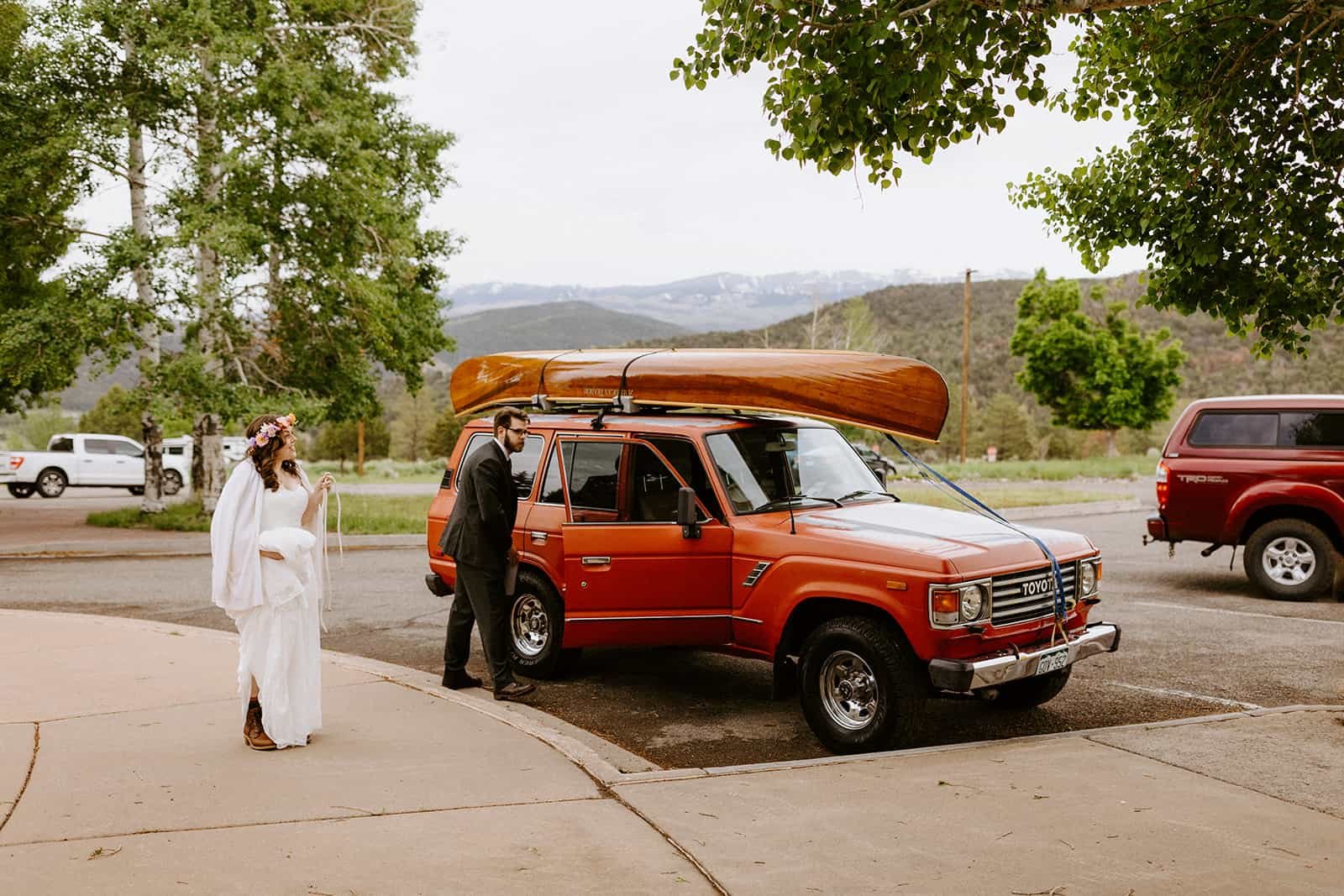 A man and woman in their wedding clothes get out of a red Toyota Land Cruiser 