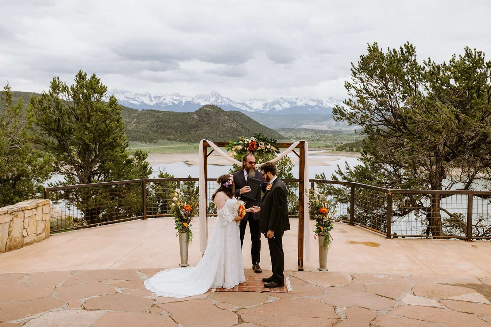 A man and woman stand in front of an arch at Ridgway State Park and the San Juan mountains in the background to get married