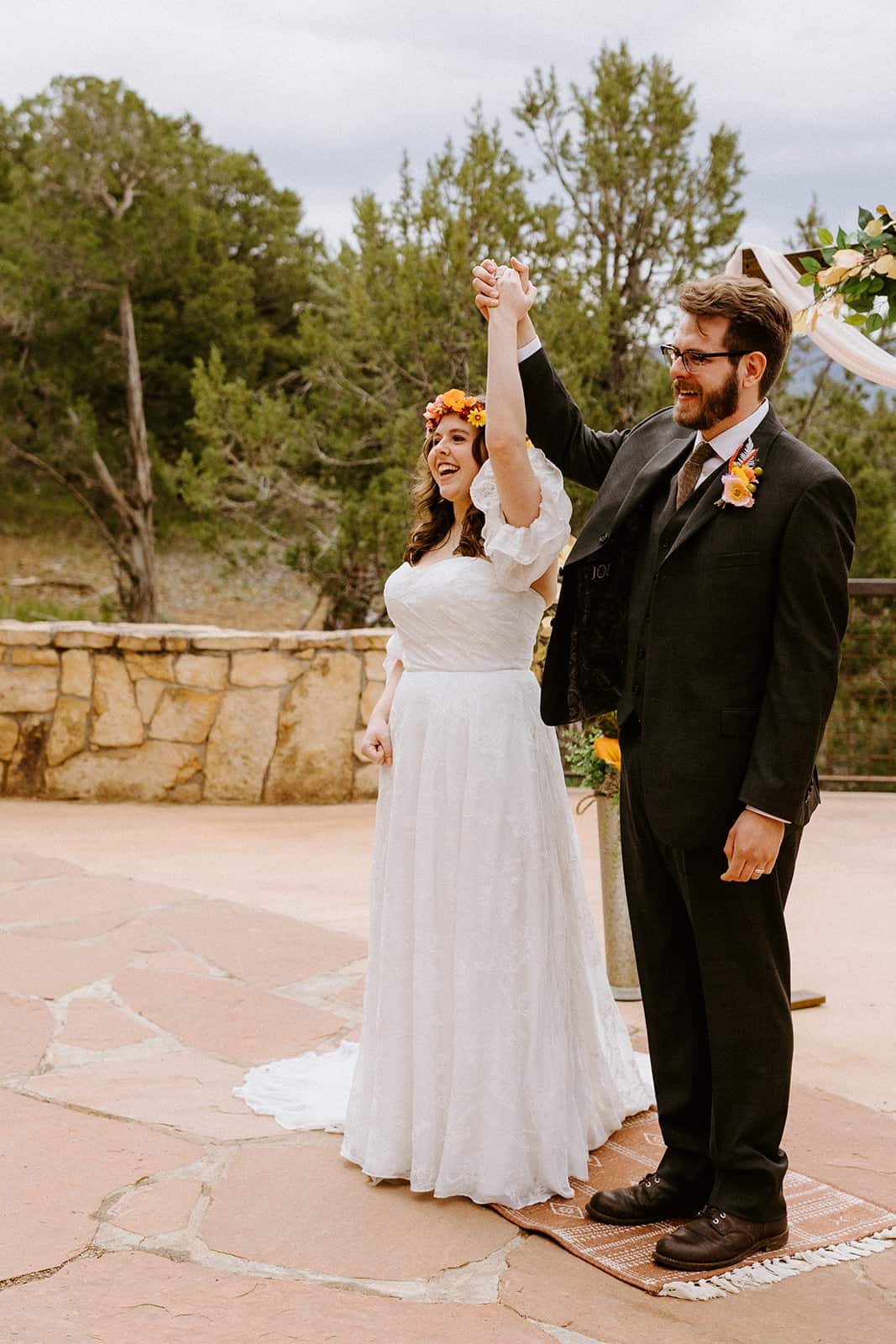 A couple stands side by side holding hands up in celebration after their wedding ceremony