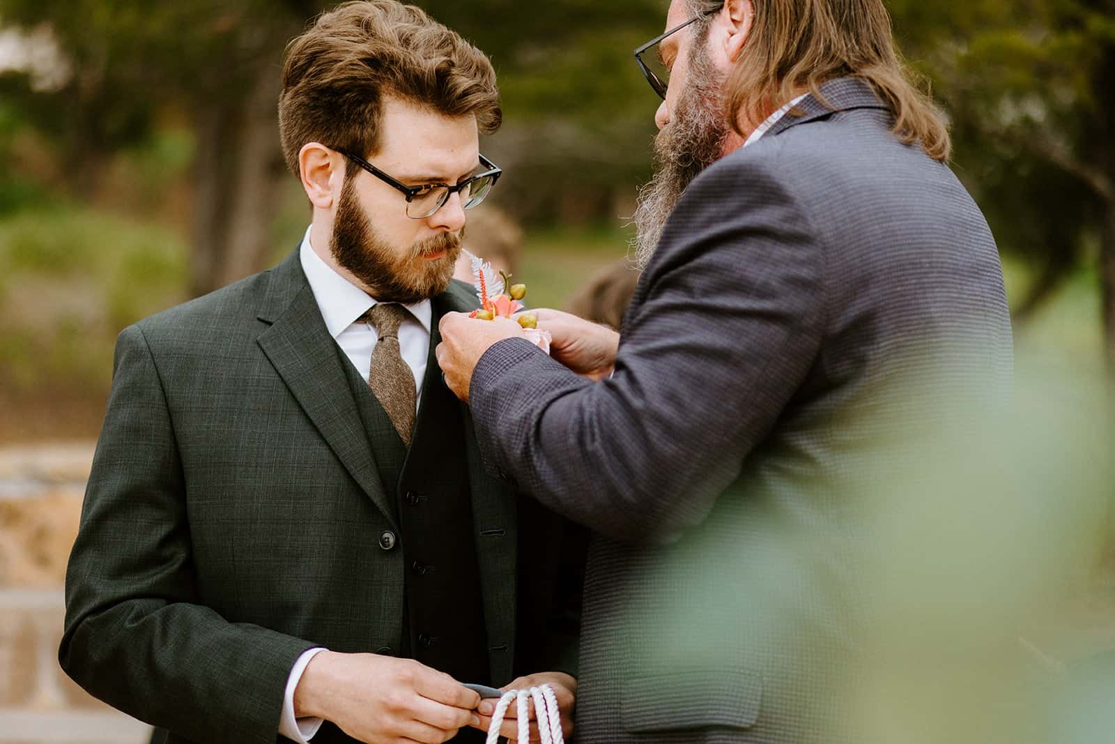 A man helps put a boutonniere on a suit jacket
