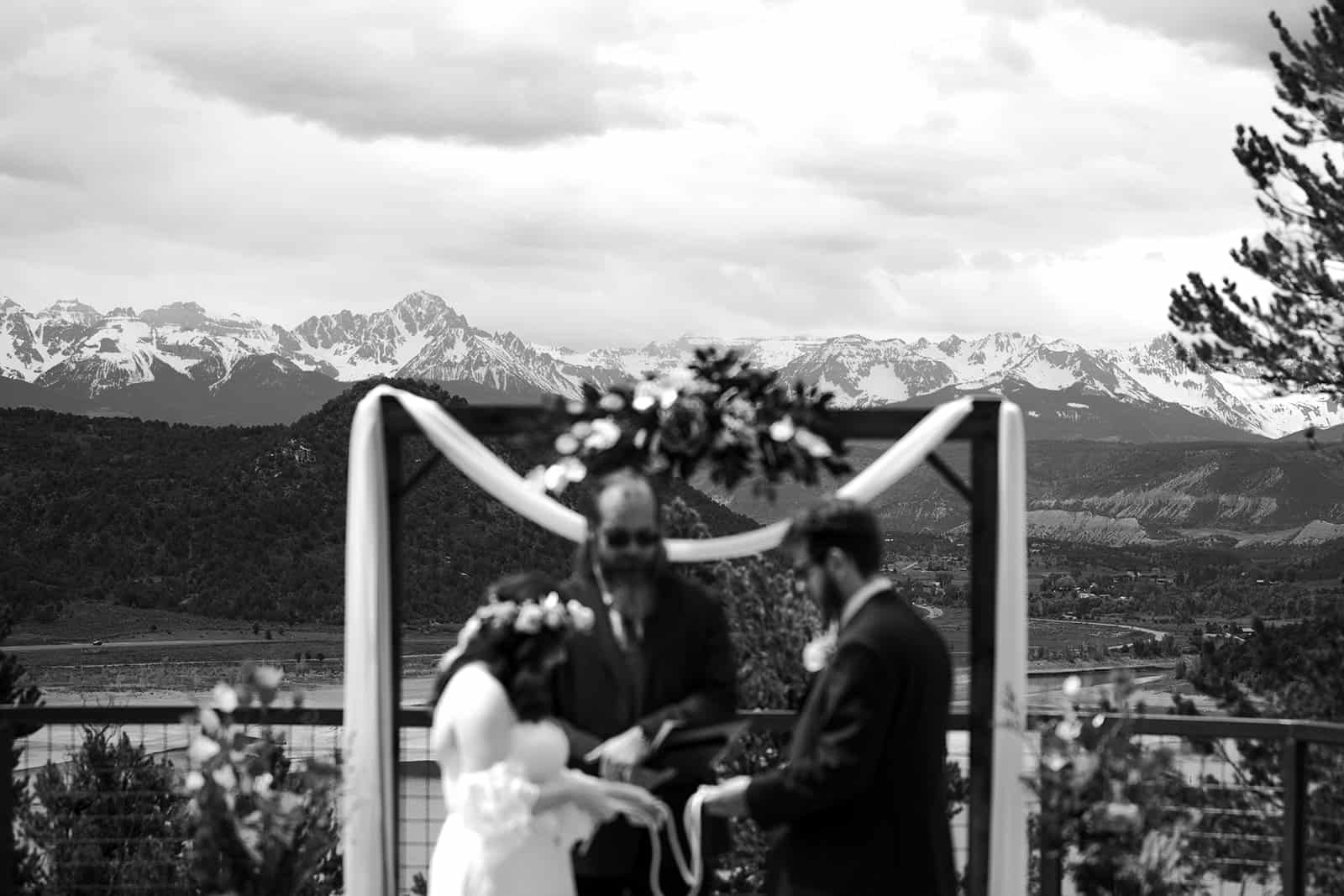 A man and woman stand in front of an arch at Ridgway State Park and the San Juan mountains in the background to get married