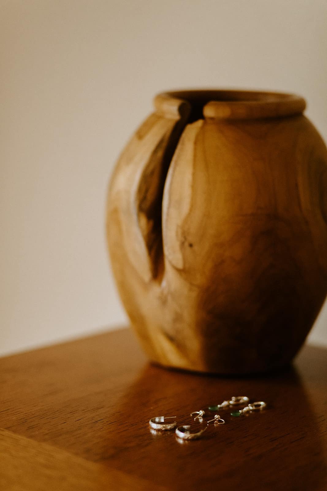 A pair of earrings sits next to a wood vase