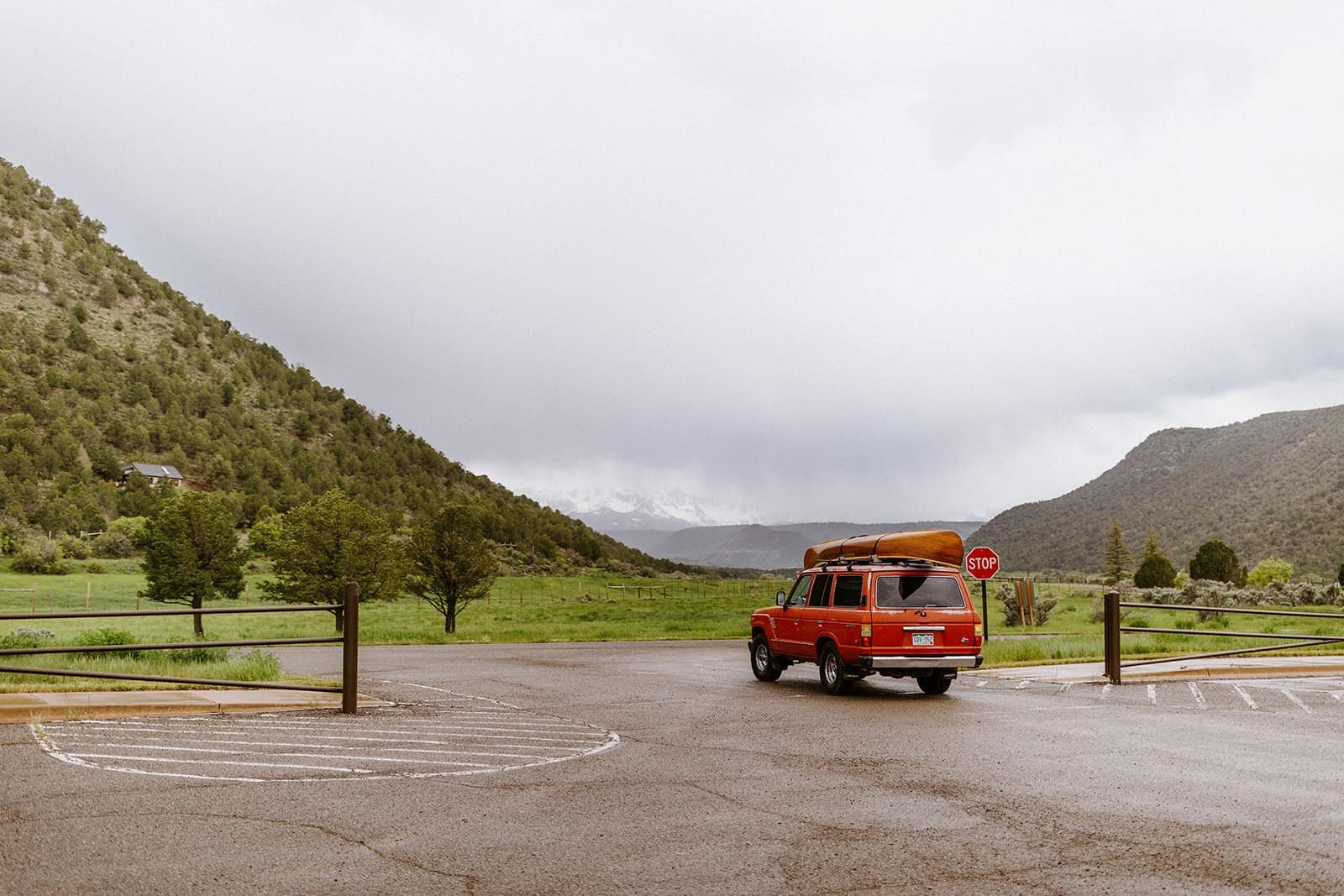 A red Toyota Land Cruiser with  a wood canoe strapped to the roof leaves Ridgway State Park