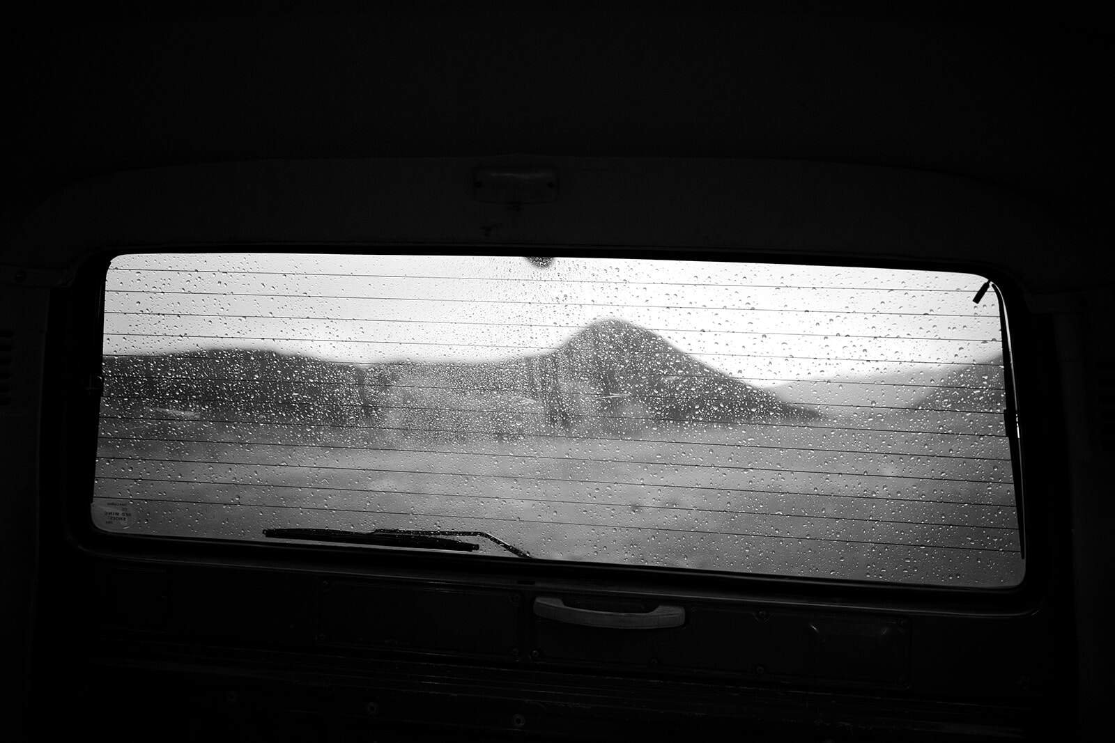 A view of mountains through the back of a rainy car windshield