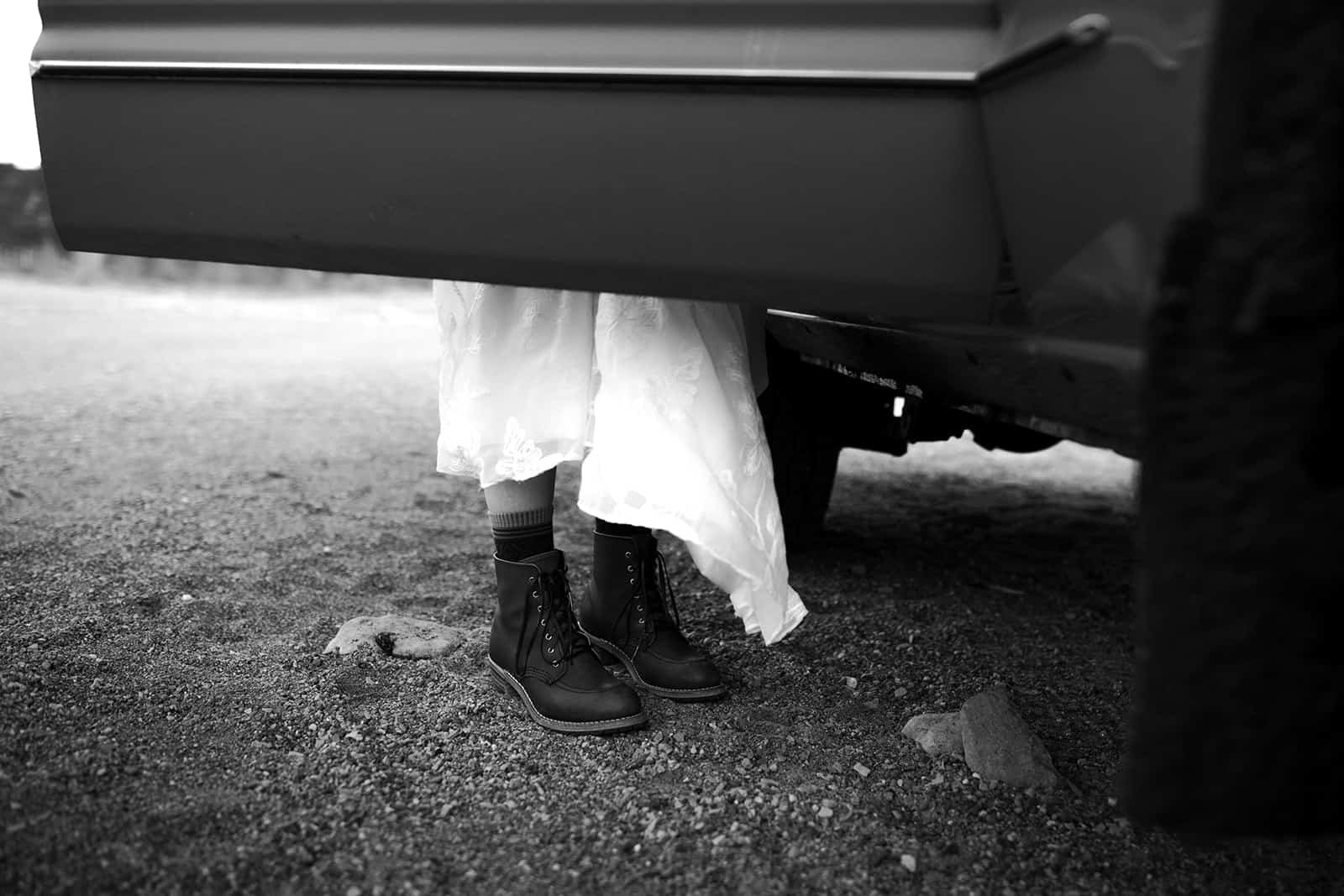 A woman in a wedding dress stands behind an open car door in her Redwing boots