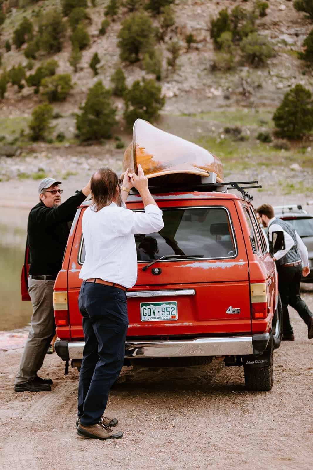 A family helps unload a wood canoe off of a red Toyota Land Cruiser