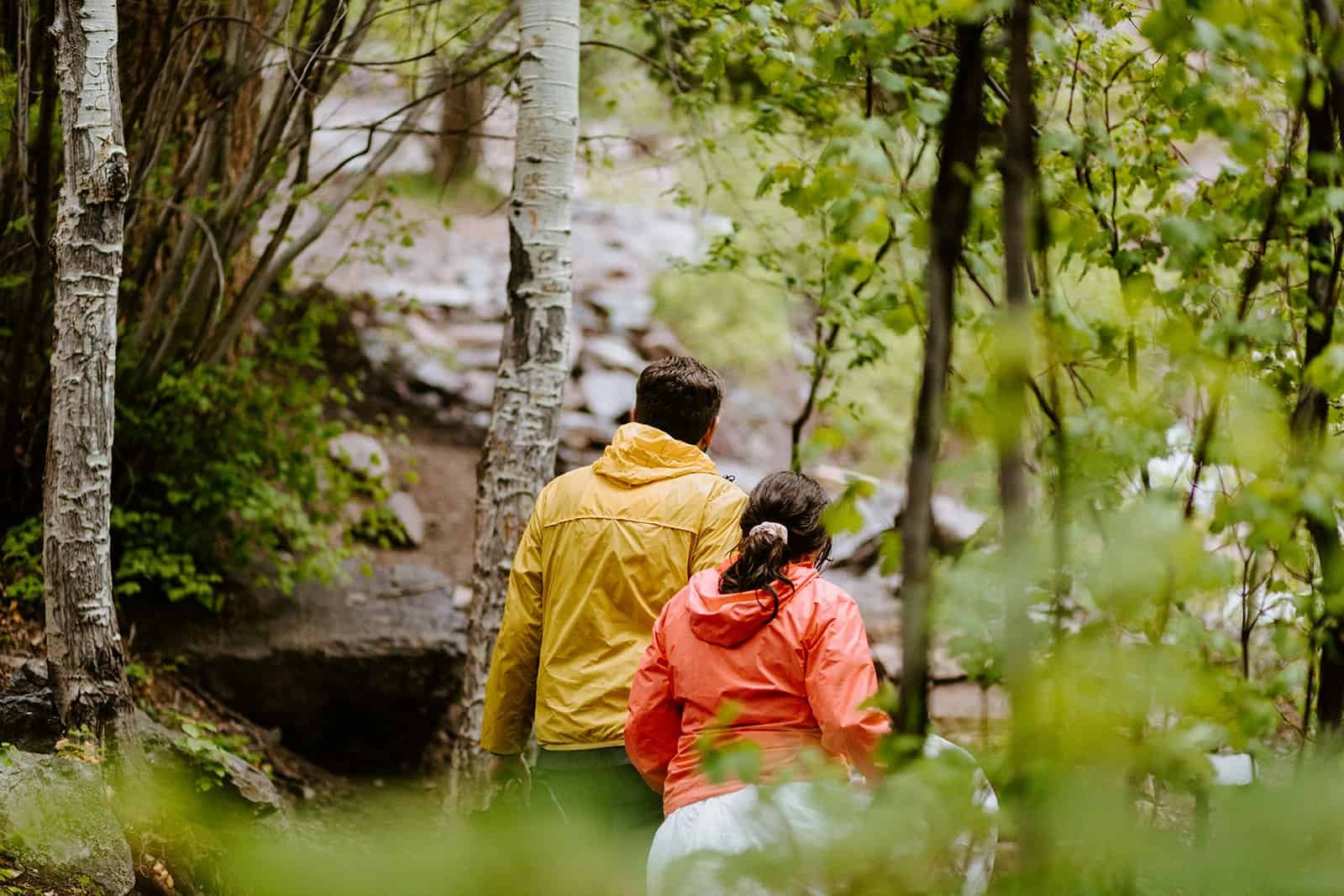 A couple in rain jackets walks in a wet forest