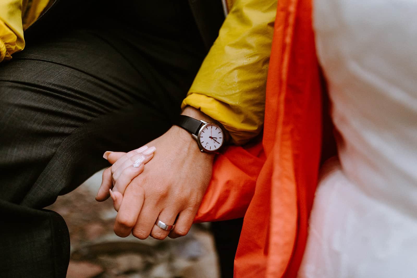 A couple in colorful rain jackets holds hands