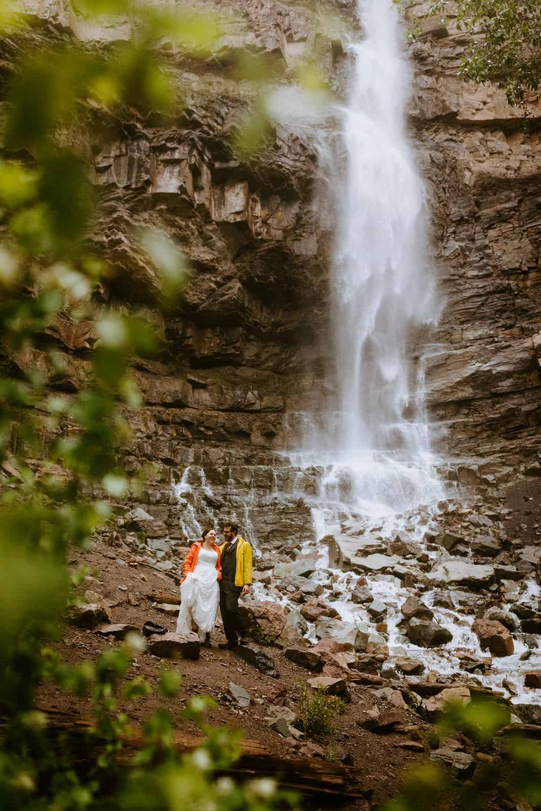 A couple in rain jackets smiles at each other at Cascade Falls in Ouray