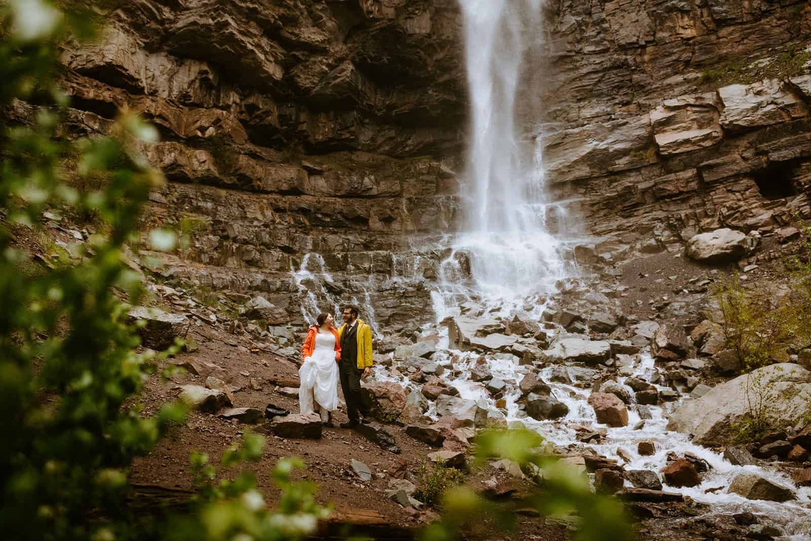 A couple in rain jackets smiles at each other at Cascade Falls in Ouray