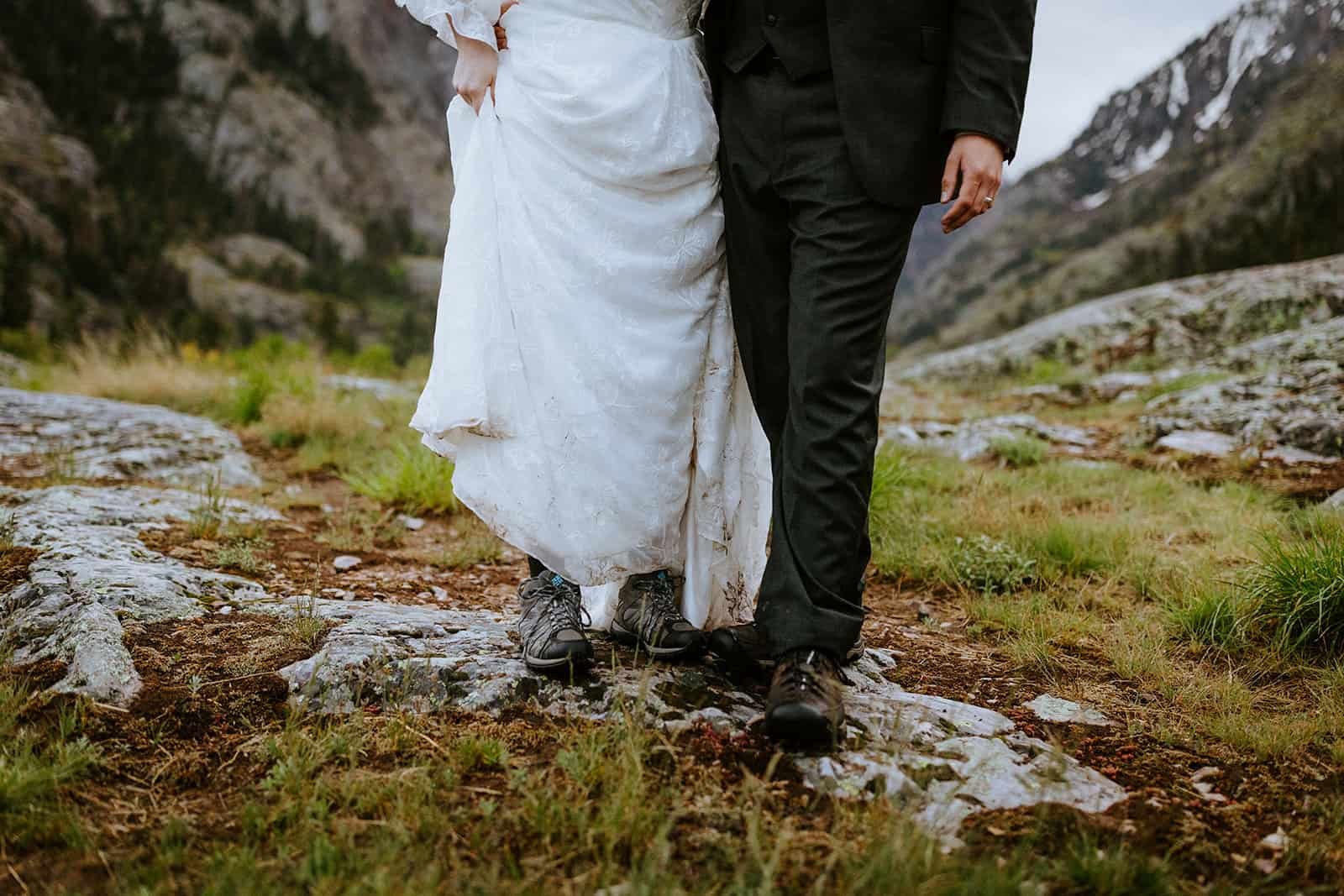 A woman in a wedding dress and man in a suit show off their Redwing boots on a rainy mountain evening
