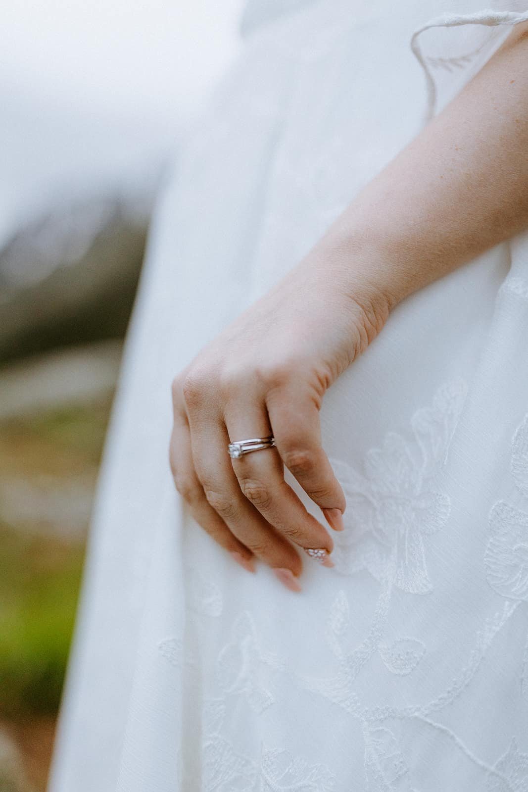 A woman's hand with a wedding ring on her finger in front of her wedding dress