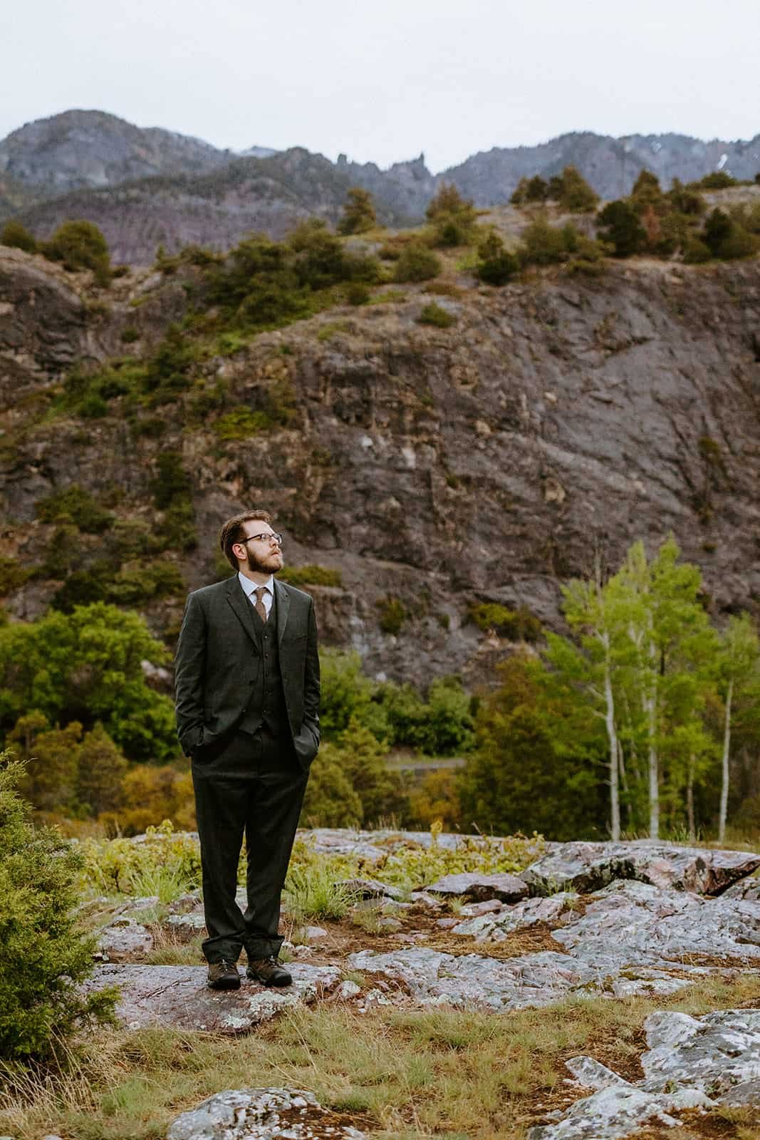 A man in a suit for his elopement looks off into the rainy mountains