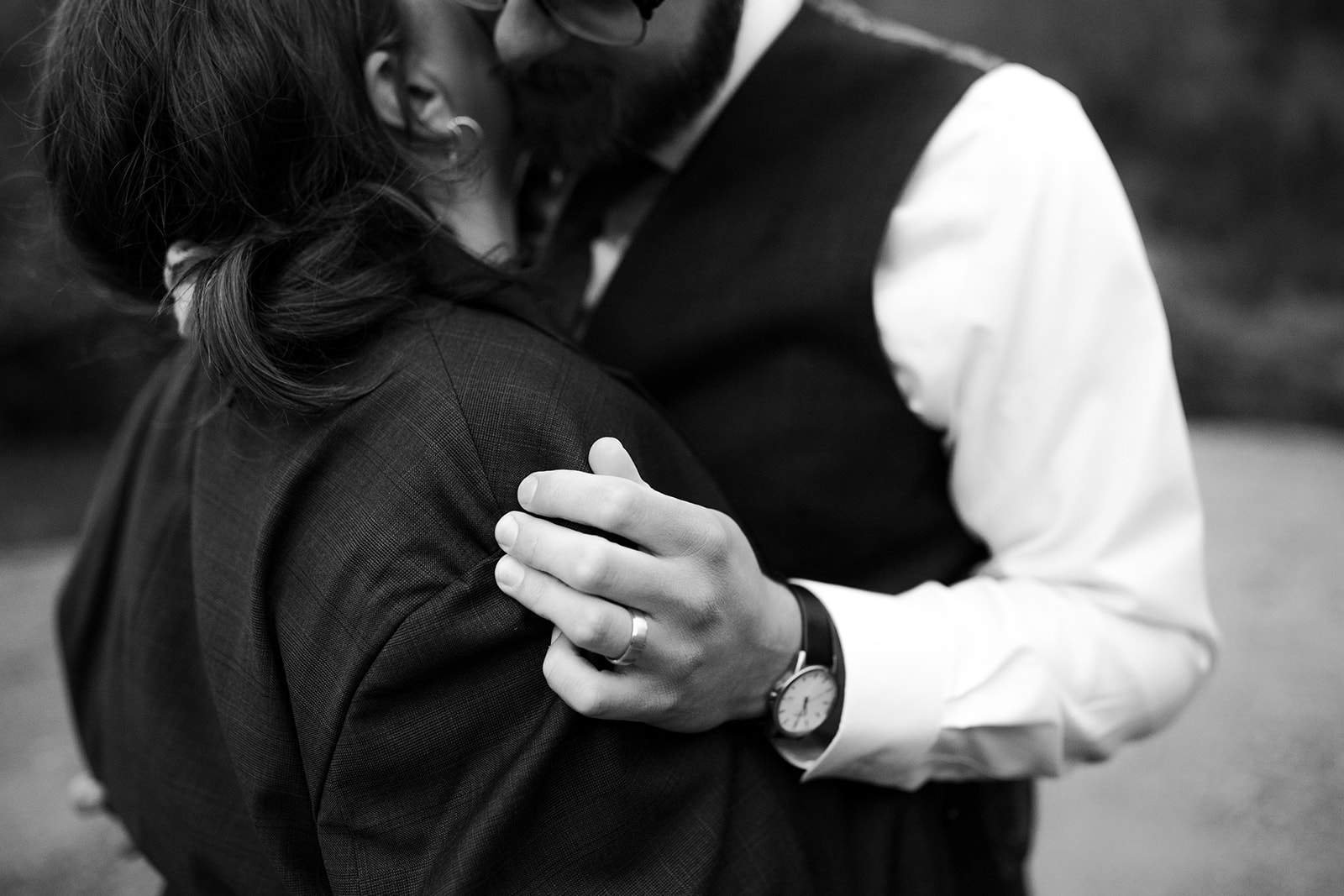 A man kisses a woman on the side of the face while she wears his suit jacket on their wedding day 