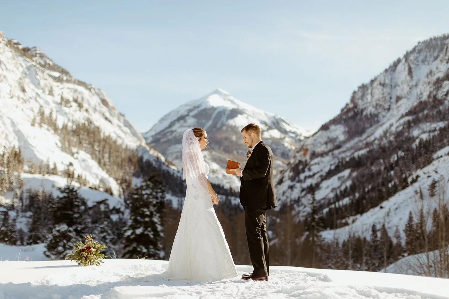 A couple reads their vows to each other in the snow with mountains behind them in Ouray