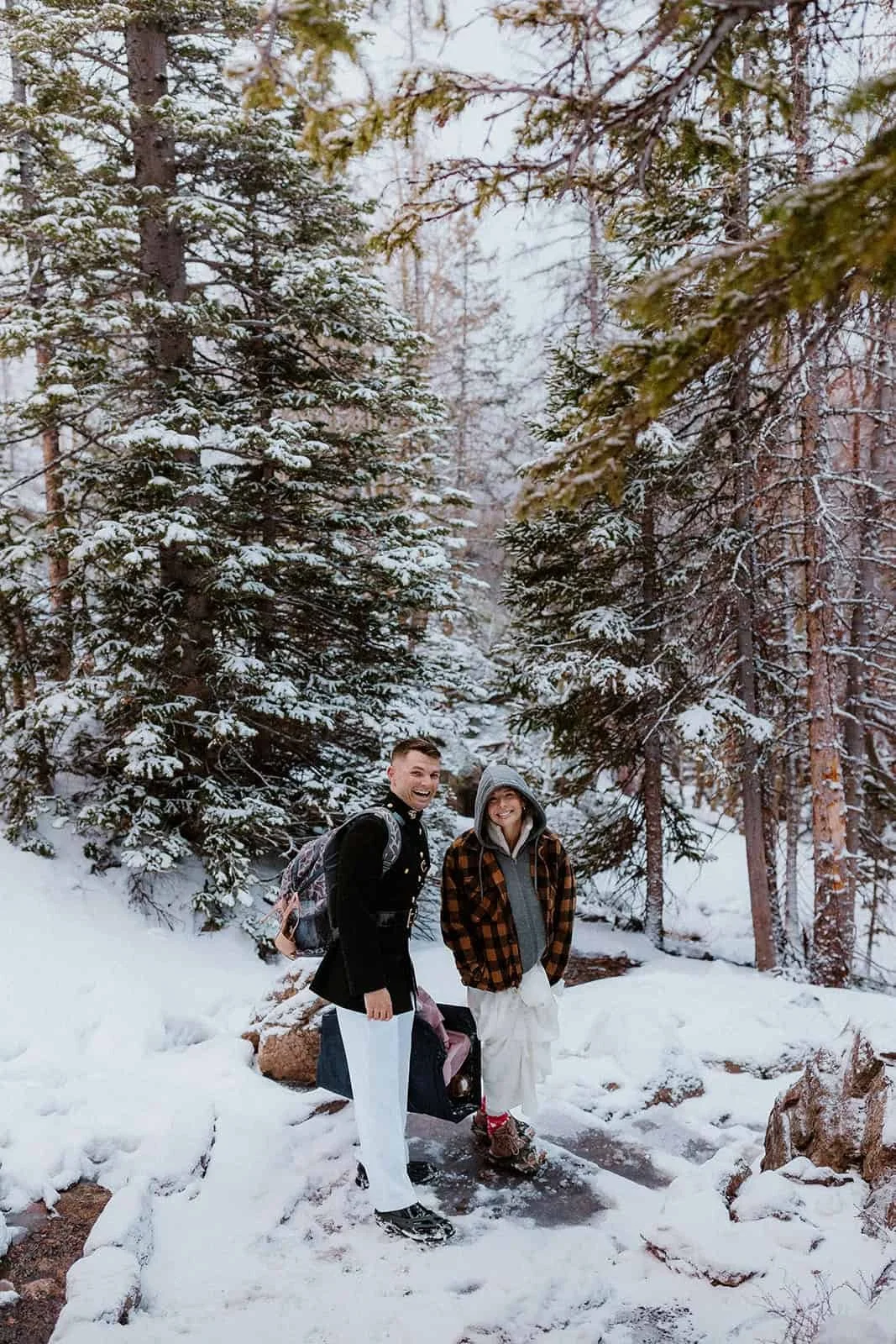 A couple in winter jackets stands on a snowy trail in the pines near Dream Lake in Rocky Mountain National Park