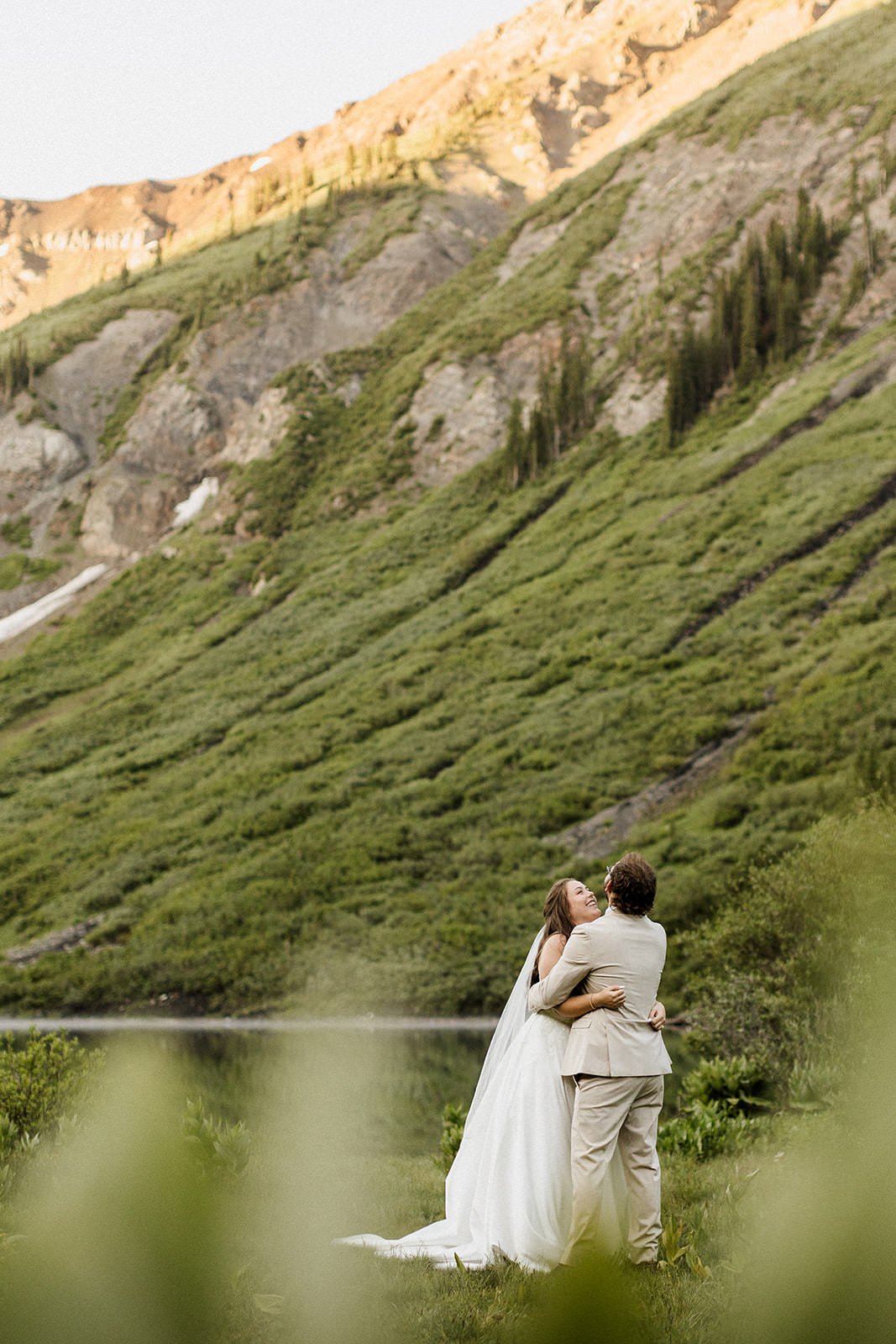 Bride and groom embracing at an alpine lake in Crested Butte with dramatic rocky mountain cliffs in the background