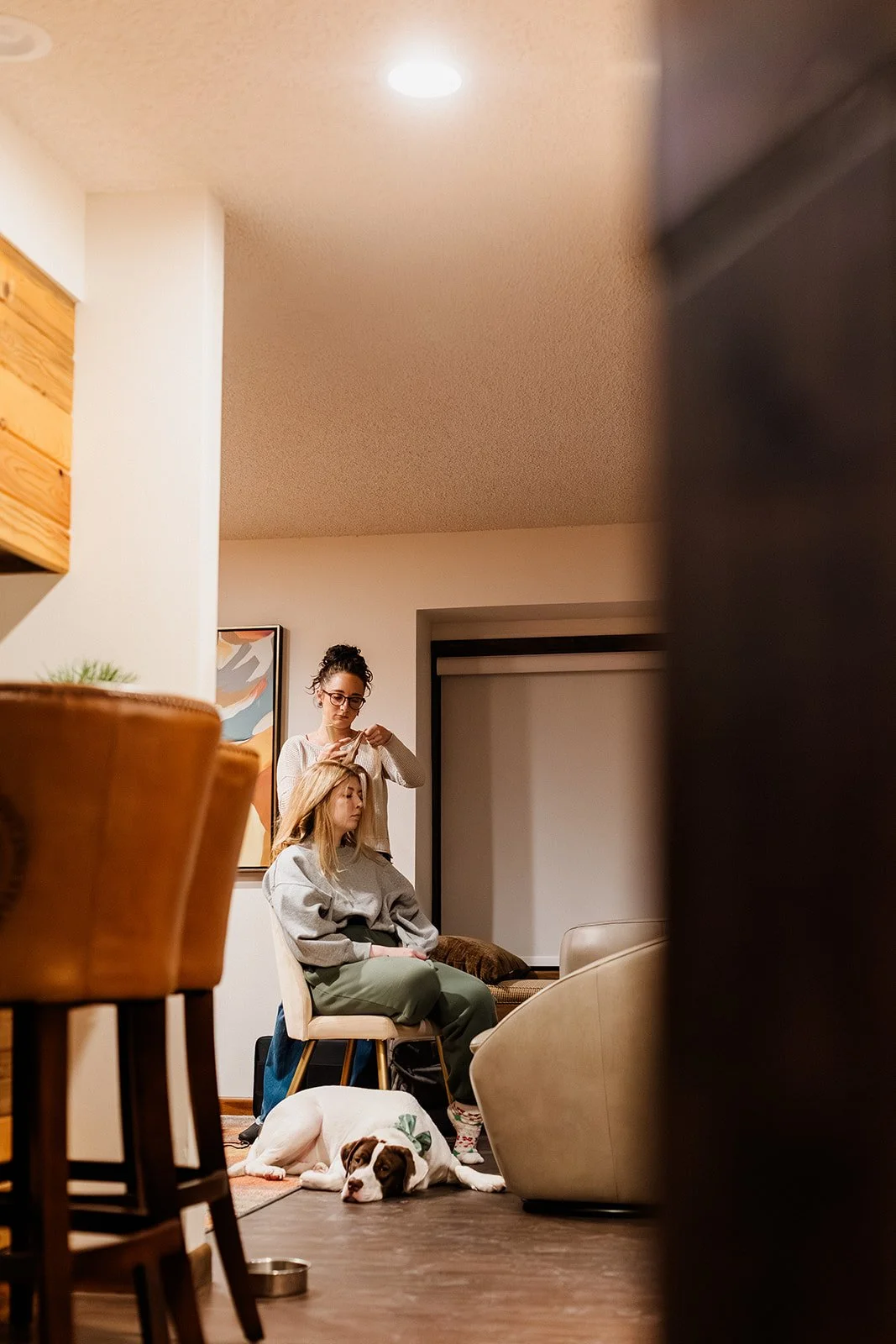 Hair stylist curling the bride's hair in a cabin living room with a dog asleep on the floor