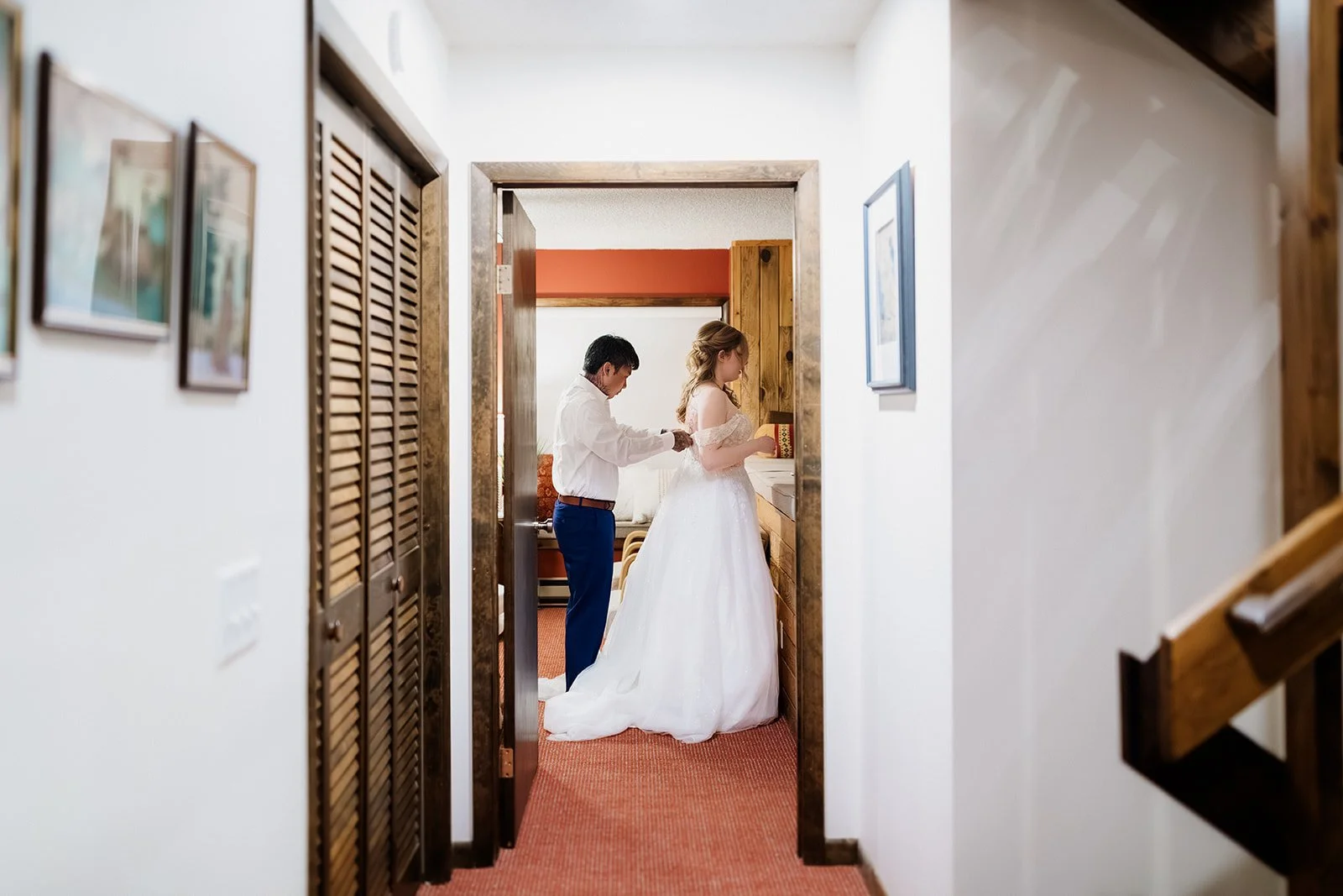 Groom helping the bride into her dress at the end of a cabin hallway