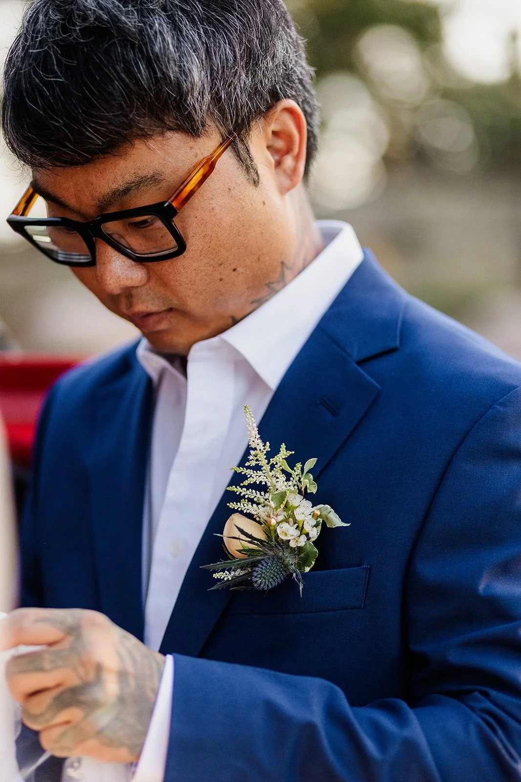 Groom in a blue suit and boutonniere looking down at his hands