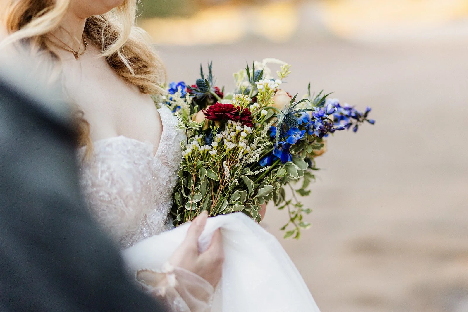 Bride holding up her dress and a wildflower bouquet of red and blue flowers