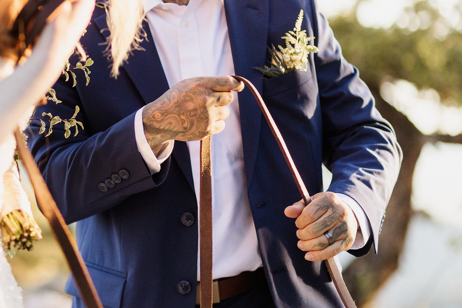 Close up of the groom's tattooed hands holding a leather dog leash