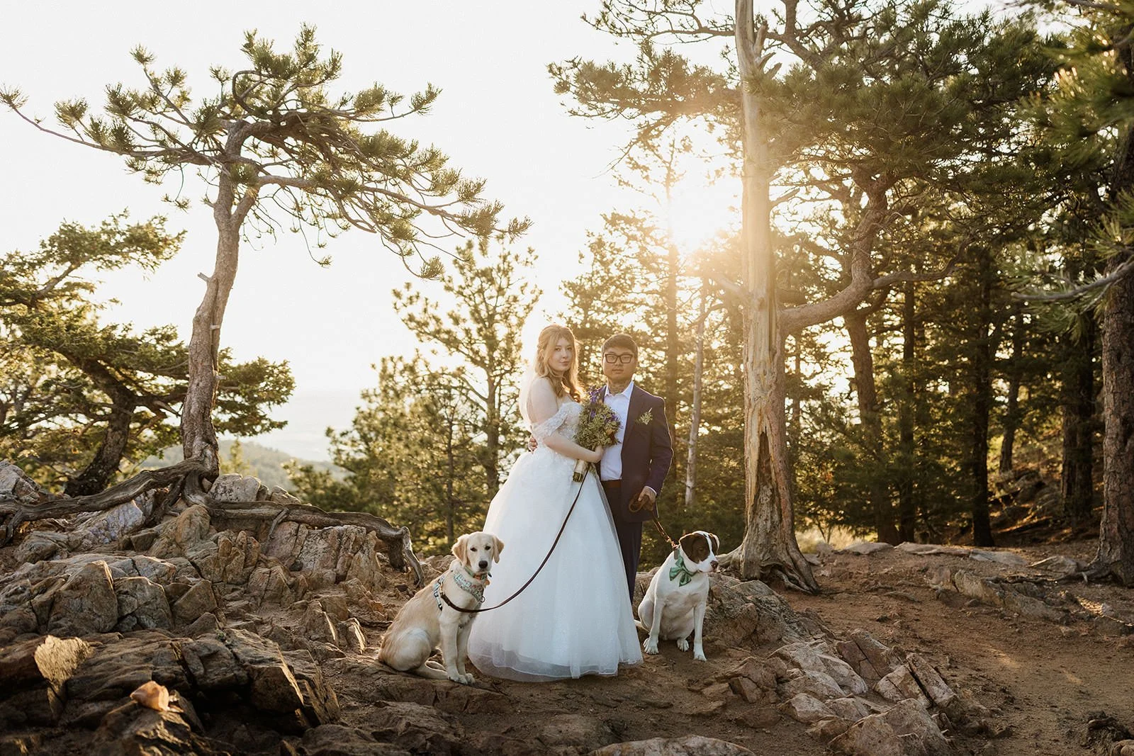 Couple standing in the pines at Lost Gulch Overlook in Boulder with their two dogs in green bow ties