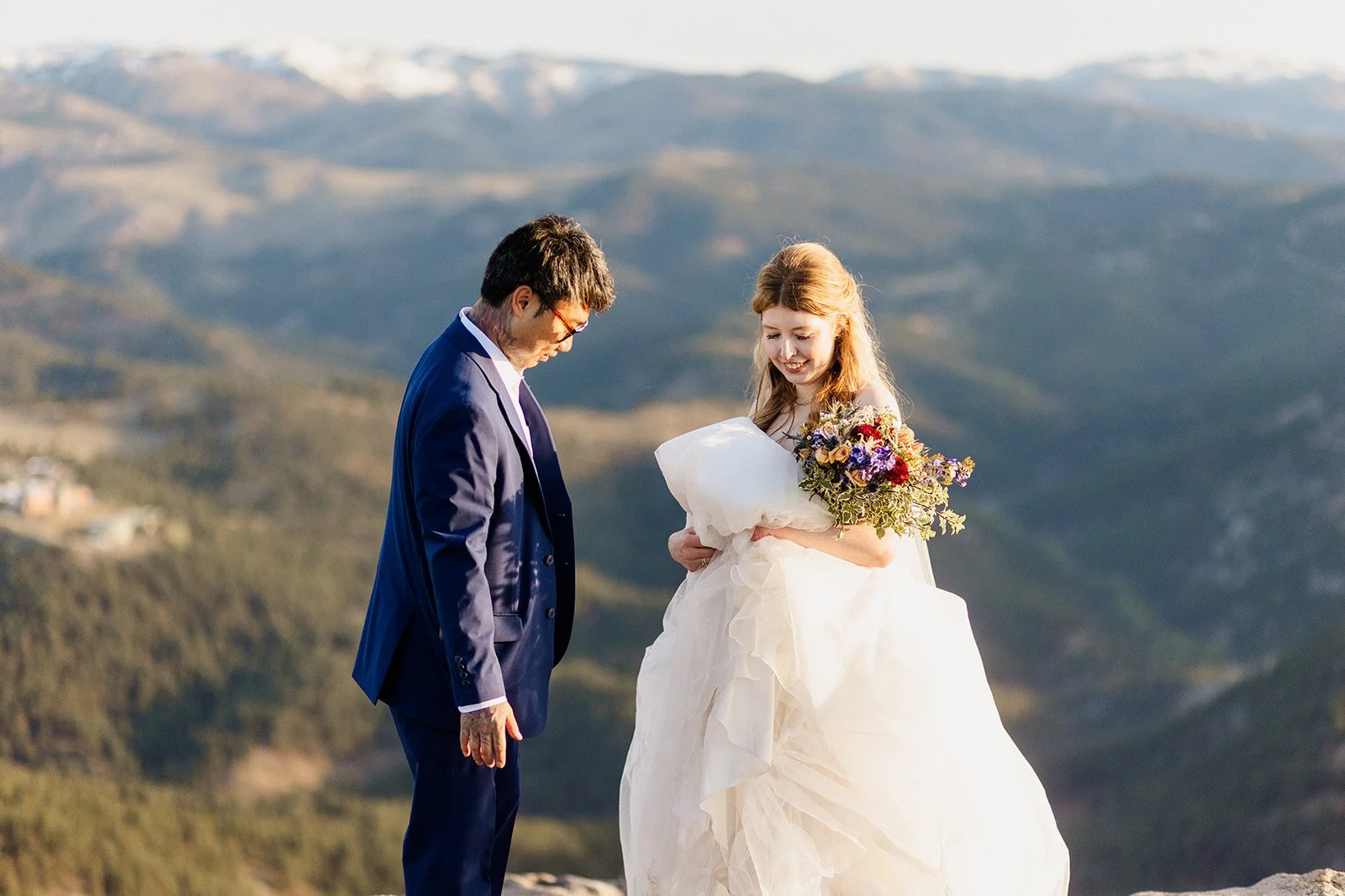 Couple laughing as she gathers up her dress above the foothills near Boulder