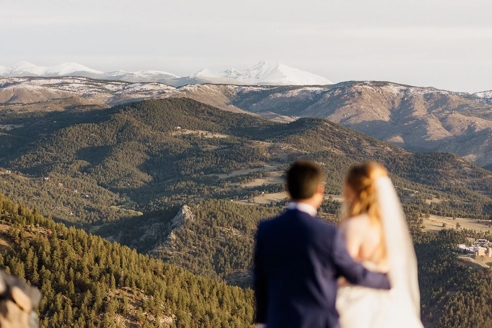 Couple with their arms around each other looking out at snow capped mountains