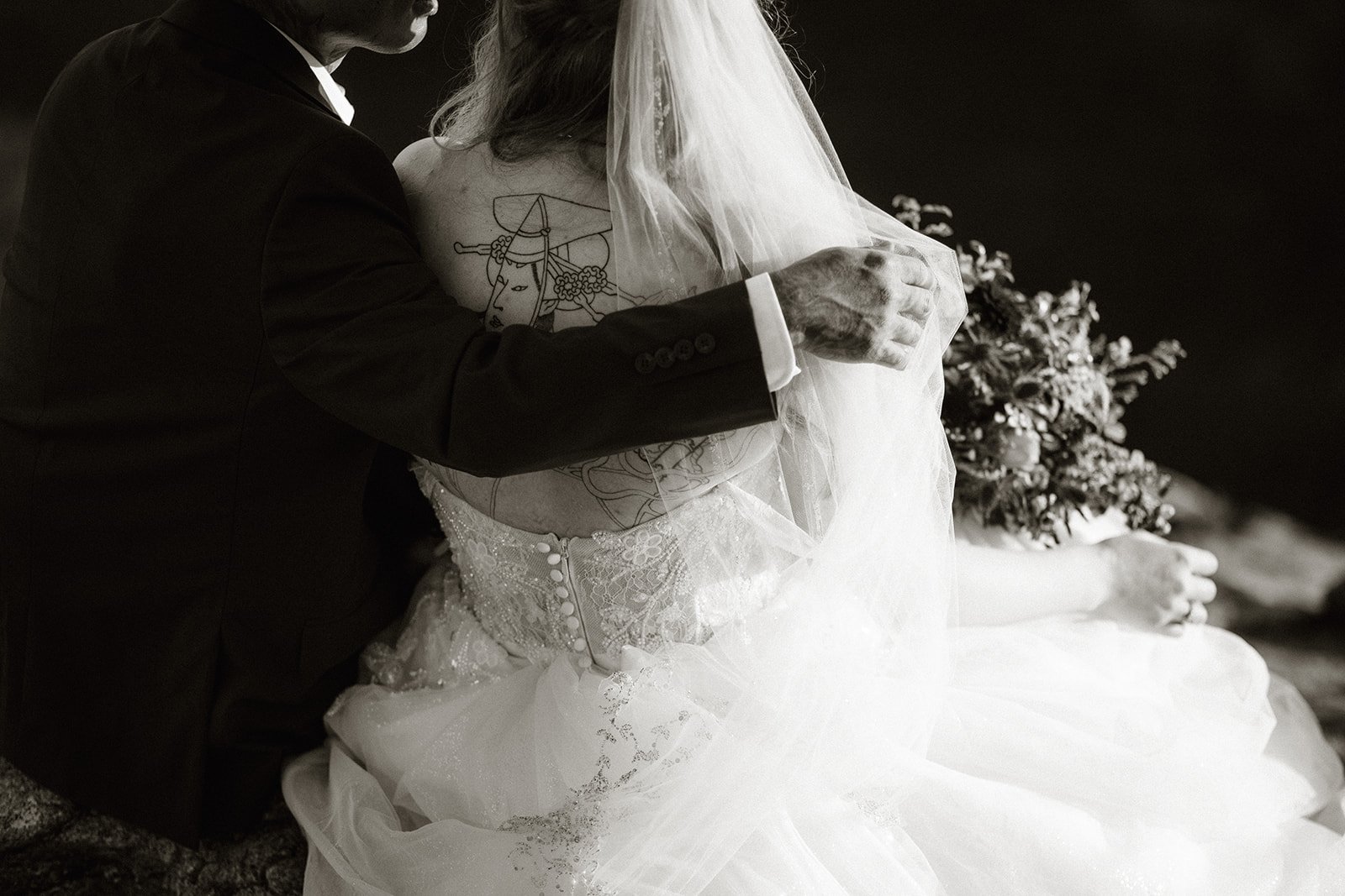 Black and white close up of the couple sitting together with her veil and bouquet