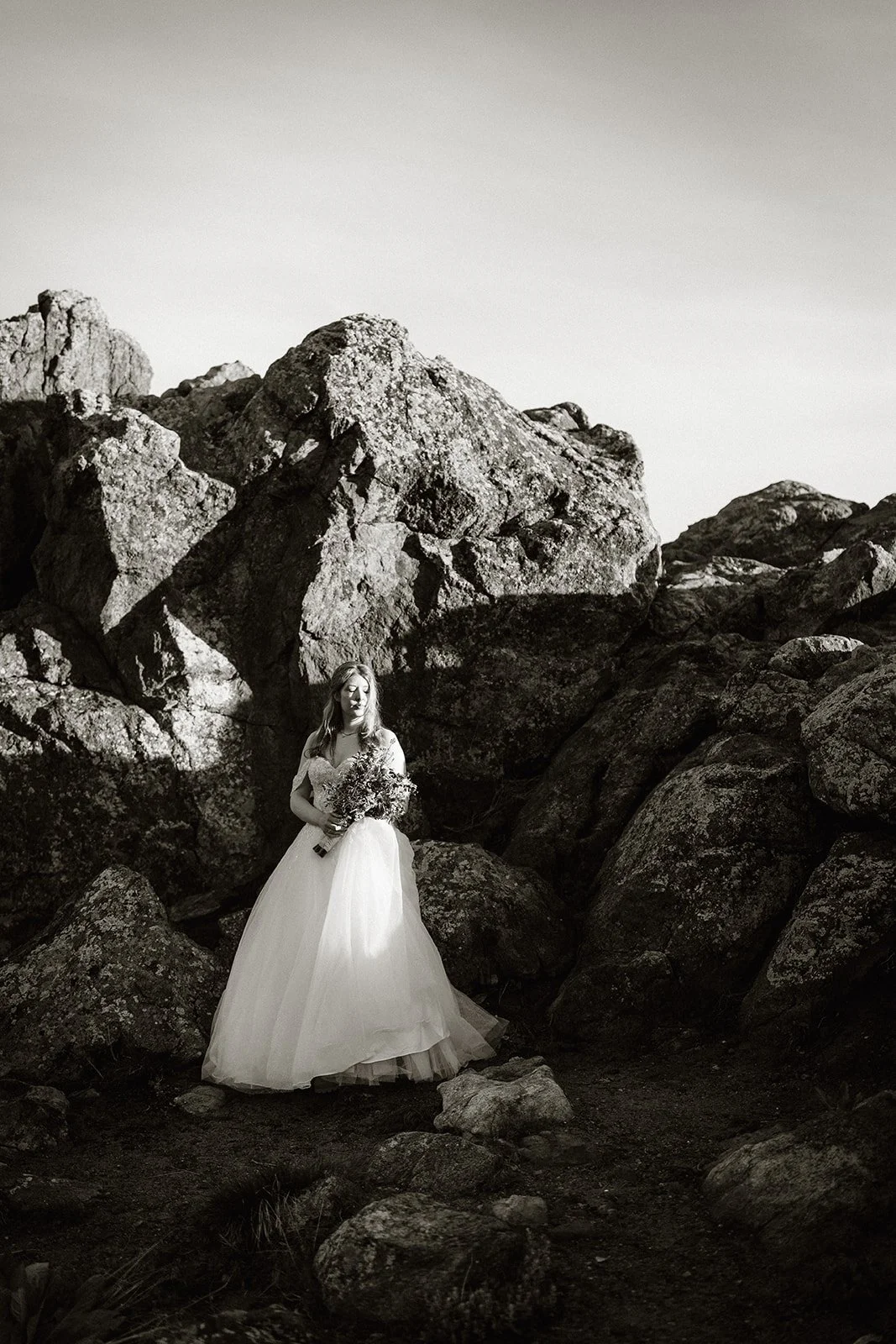 Bride standing among large boulders, in black and white