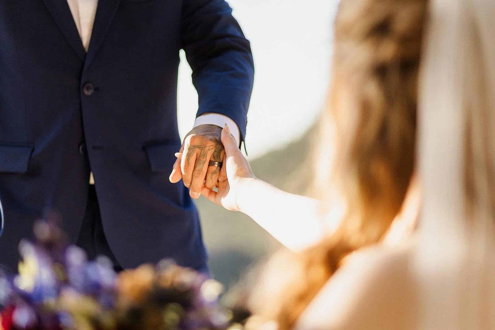 Couple holding hands with the bouquet blurred in the foreground