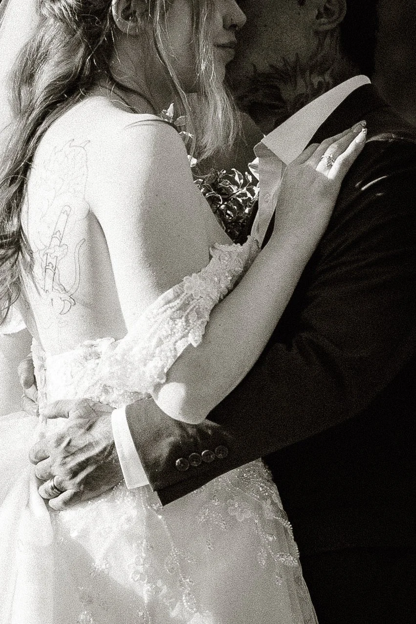 Black and white close up of the couple embracing, her back tattoo showing