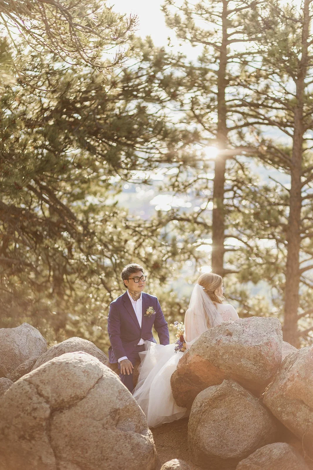 Couple sitting among boulders under tall pines in hazy morning light