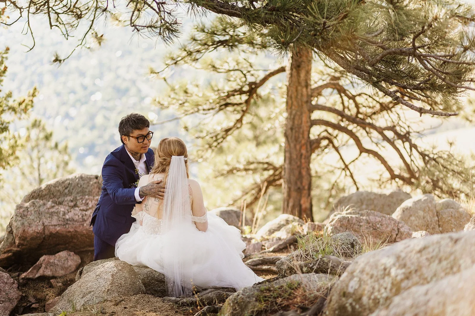 Groom with his arm around the bride as they sit on the rocks