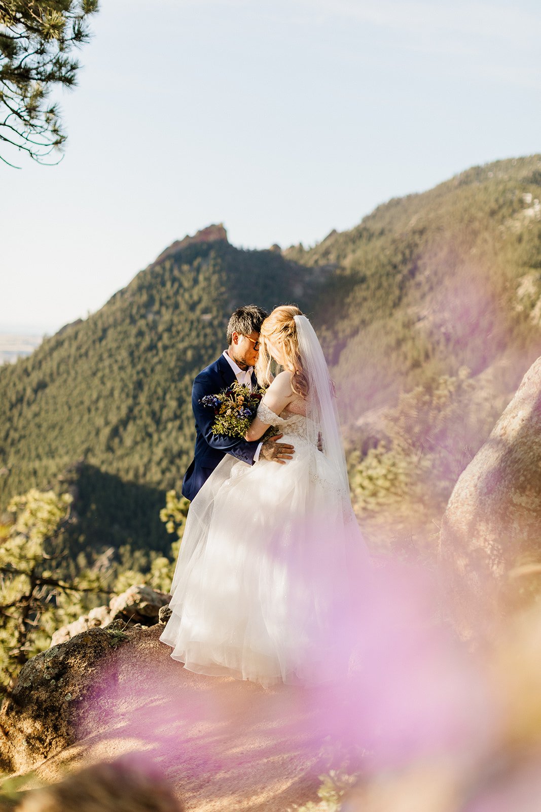 Couple kissing on a ledge above Boulder, framed by pink wildflowers