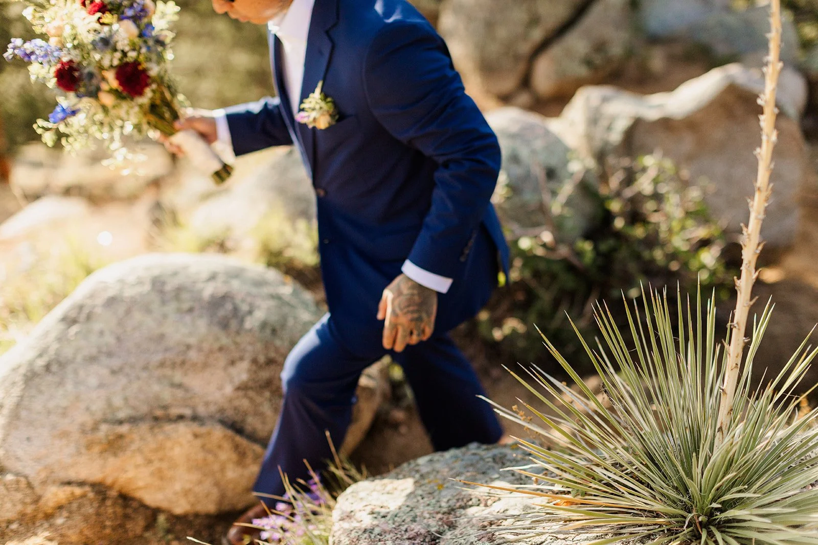 Groom stepping over boulders carrying the bride's bouquet