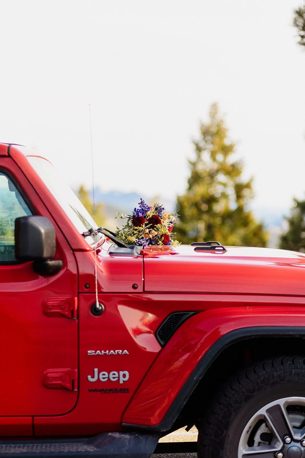 Red Jeep parked in the pines with the wedding bouquet on the dashboard