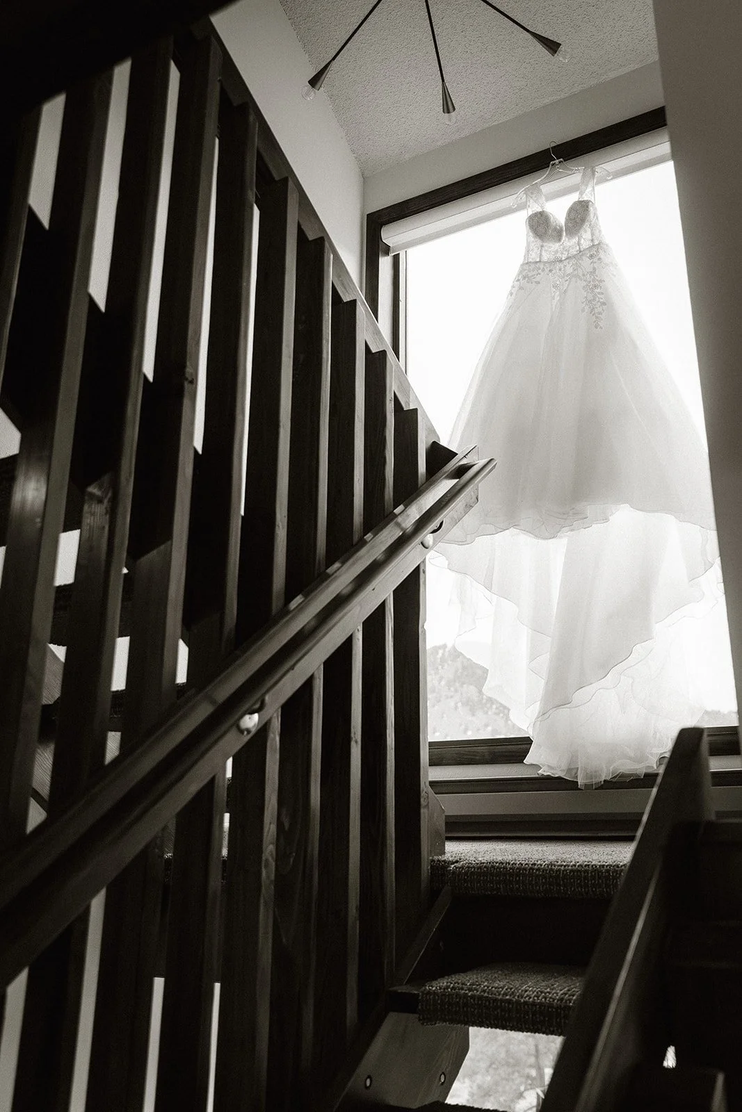 Wedding dress hanging in a stairwell window, in black and white