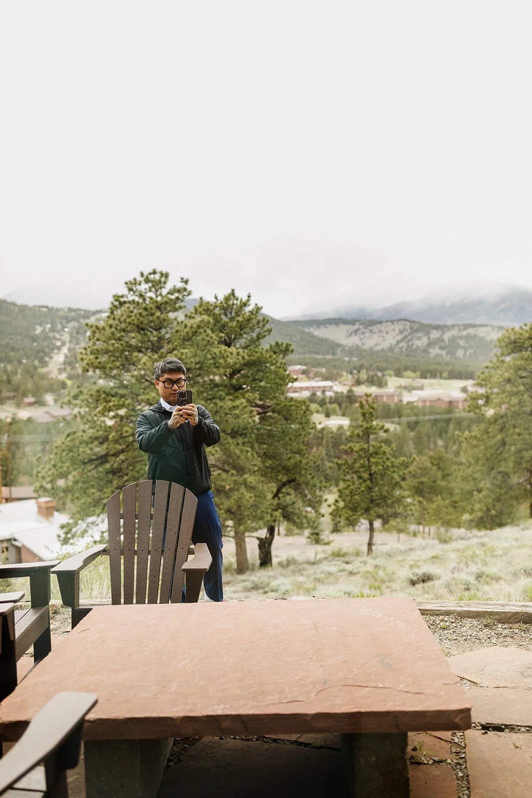 Groom taking a photo of his wife from the patio of a cabin overlooking Estes Park
