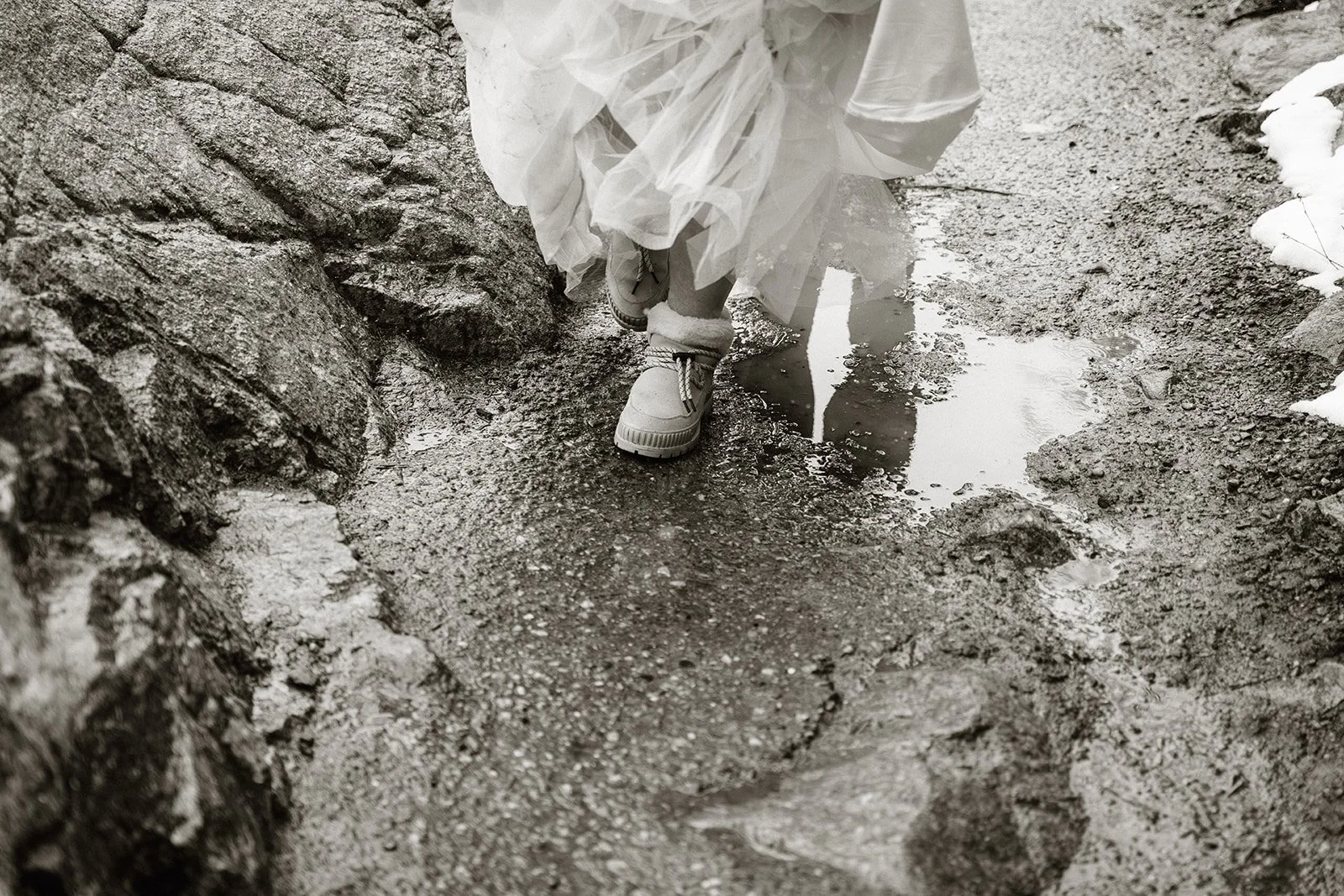 Black and white close up of the bride's boots on the wet trail