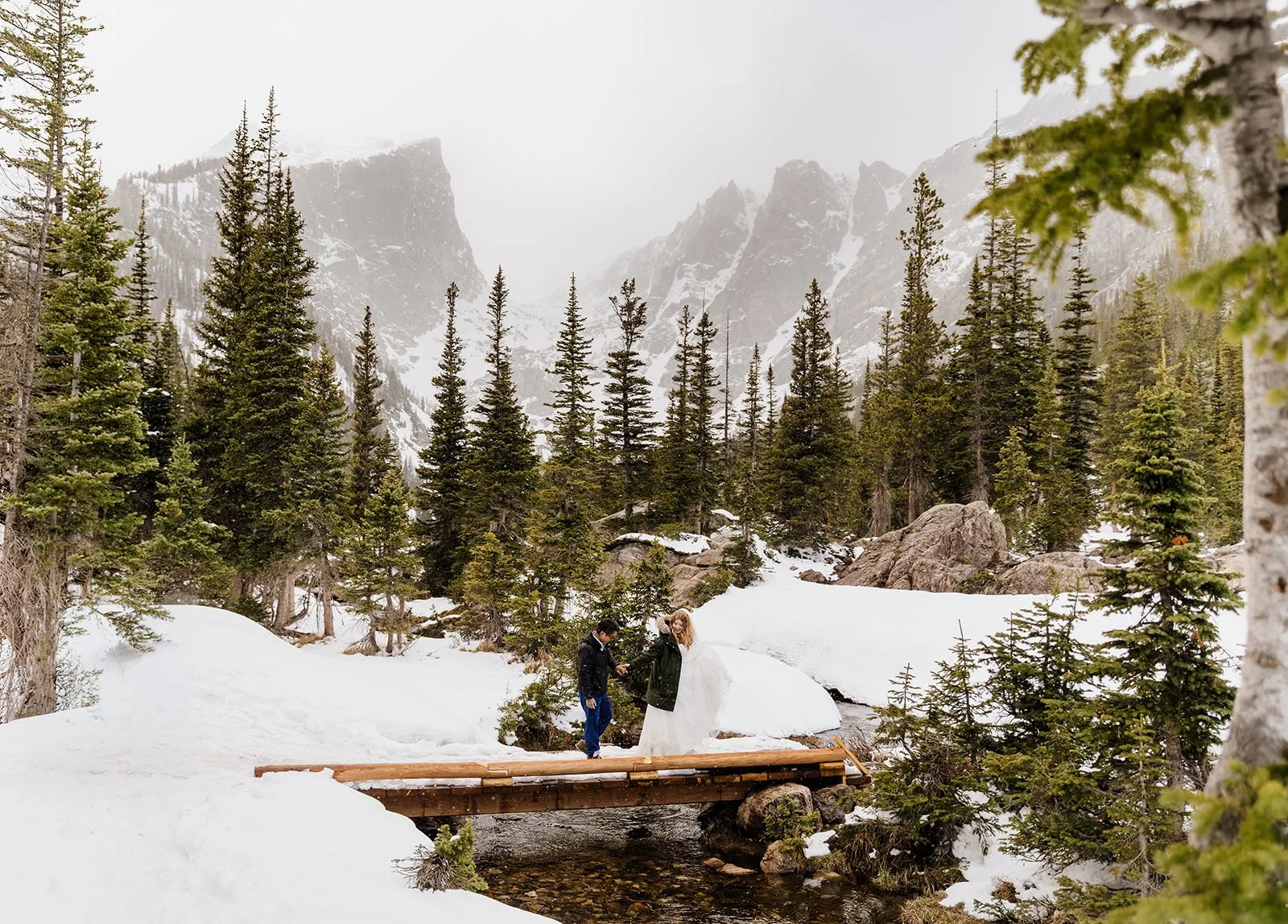 Couple crossing a log bridge over deep snow near Dream Lake