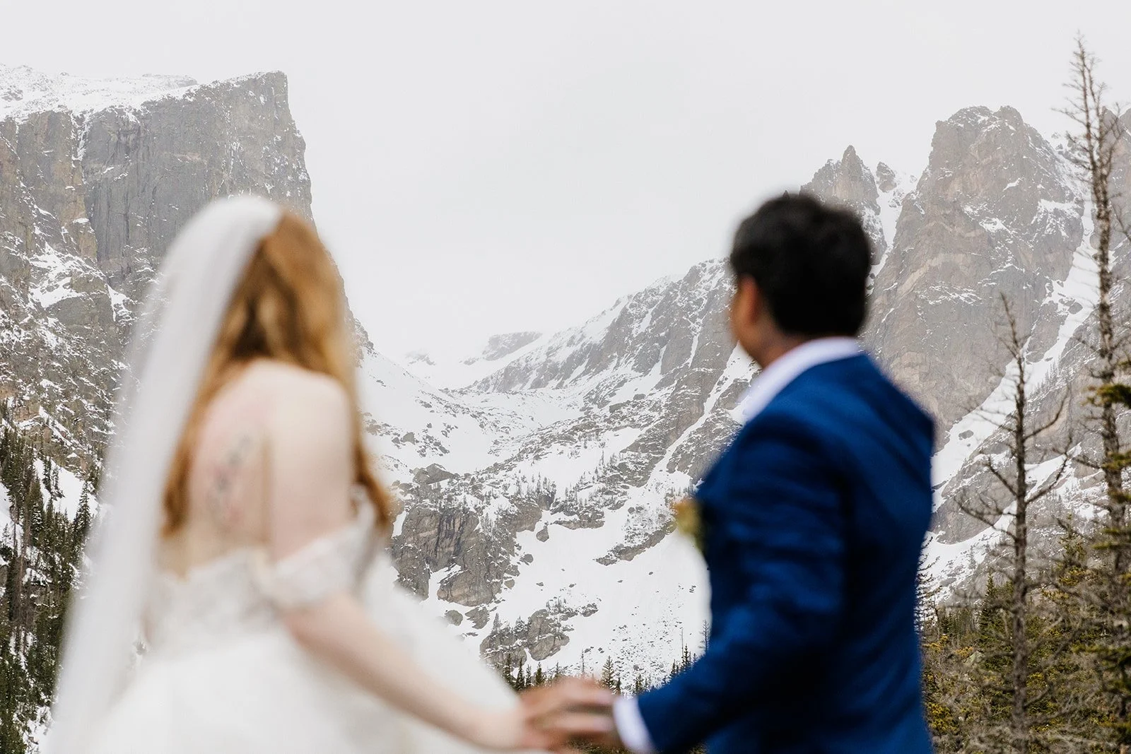 Couple holding hands and facing the snowy peaks above Dream Lake