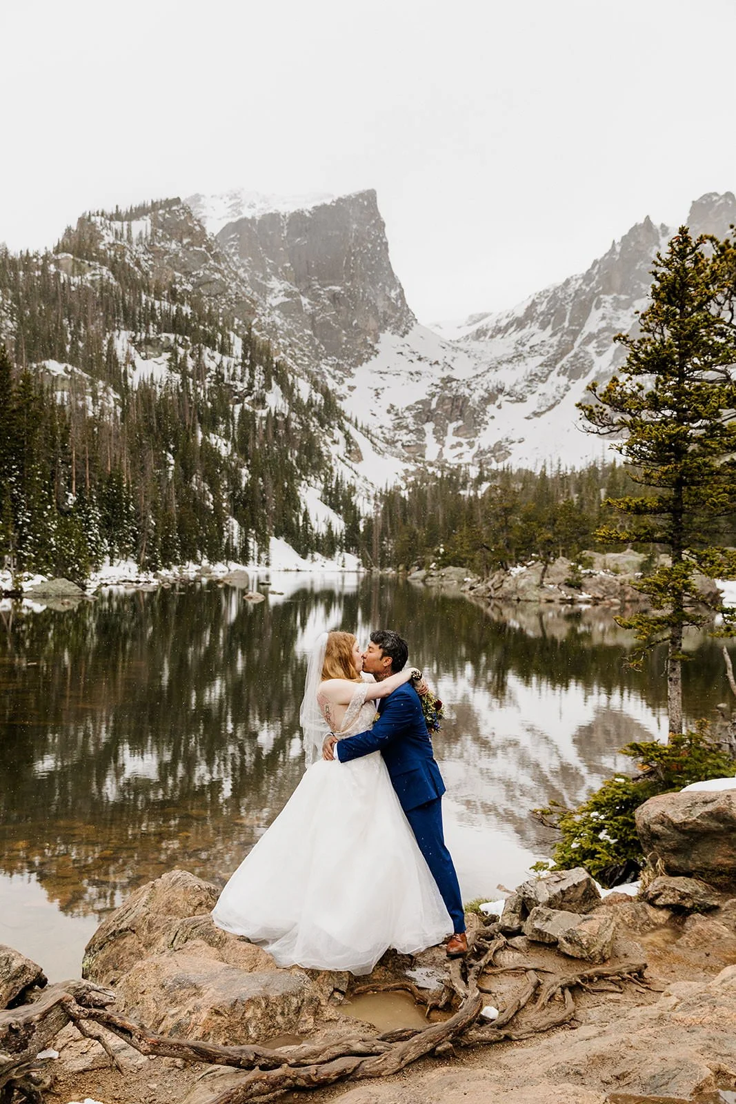 Couple kissing on the shore of Dream Lake with Hallett Peak reflected in the water